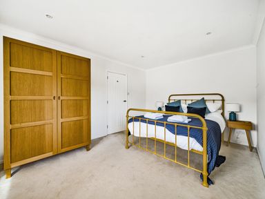 A bedroom with a yellow metal bed with blue bedding a wooden wardrobe and two side tables with lamps at Fairwinds in Portreath
