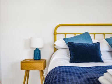 A bedroom with a yellow metal bed frame blue pillows blue lamp on a wooden bedside table at Fairwinds in Portreath