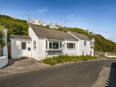 A white detached house with bay windows on a hillside road at Fairwinds in Portreath