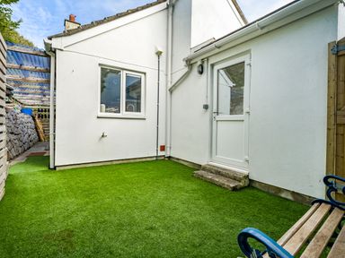 A small fenced yard with artificial grass a bench and a white door at Fairwinds in Portreath