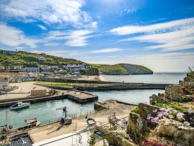 A harbor with boats docked near a beach and houses on a hill with cliffs and the sea in the background at Fairwinds in Portreath