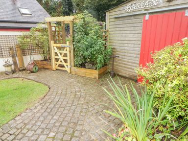 A garden area with a cobblestone path a wooden gate plants and a shed with a red door at St Dogwells Barn near Wolfscastle