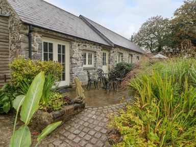 An outdoor patio area with metal chairs and table in front of a stone building with plants and cobblestone path at St Dogwells Barn near Wolfscastle