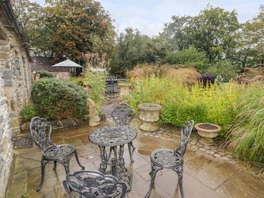 A stone patio with metal garden furniture and plants near a stone wall at St Dogwells Barn near Wolfscastle