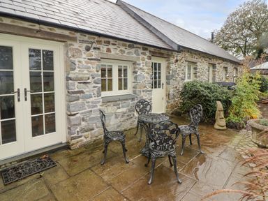 An outdoor patio with a metal table and four chairs next to a stone building with white doors and windows at St Dogwells Barn near Wolfscastle