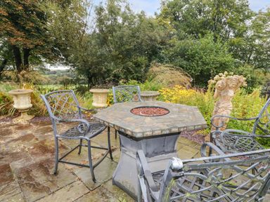 An outdoor patio with metal chairs a hexagonal table and garden statues surrounded by plants at St Dogwells Barn near Wolfscastle