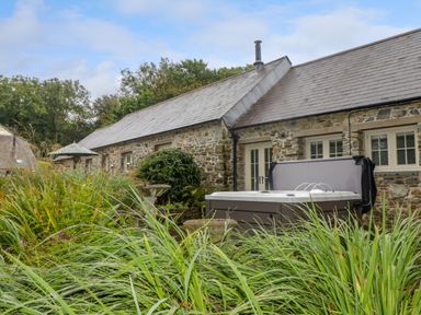 An outdoor view of a stone building with slate roof with a hot tub and garden near St Dogwells Barn near Wolfscastle