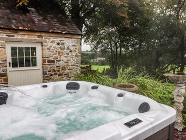 An outdoor hot tub with bubbling water next to a stone building and garden at St Dogwells Barn near Wolfscastle