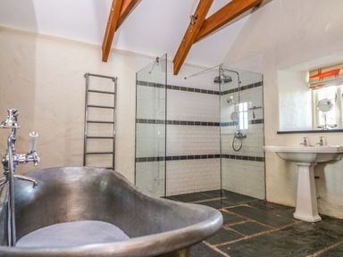 A bathroom with a metal bathtub a glass shower enclosure a white pedestal sink and exposed wooden beams at St Dogwells Barn near Wolfscastle