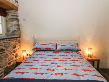A bed with fox patterned bedding between two wooden nightstands with lamps at St Dogwells Barn near Wolfscastle