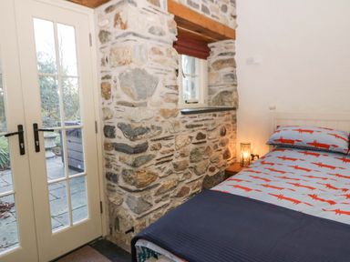 A bedroom with a single bed next to a stone wall and glass doors at St Dogwells Barn near Wolfscastle