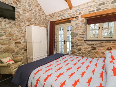 A bedroom with a bed covered in fox patterned bedding an armchair a white wardrobe stone walls and windows at St Dogwells Barn near Wolfscastle
