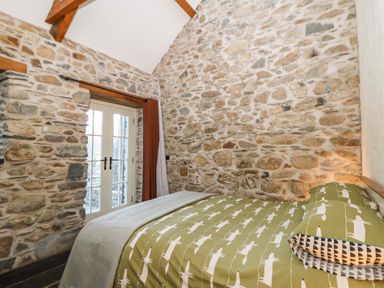 A bedroom with a green patterned bedspread stone walls and a door with curtains at St Dogwells Barn near Wolfscastle