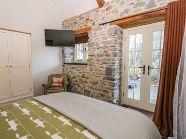 A bedroom with a bed a wardrobe an armchair a wall mounted tv and glass doors at St Dogwells Barn near Wolfscastle