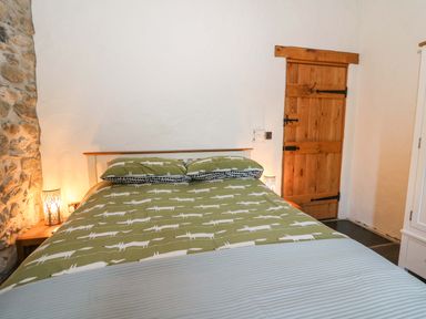 A bedroom with a double bed with patterned bedding beside two bedside tables with lamps and a wooden door at St Dogwells Barn near Wolfscastle