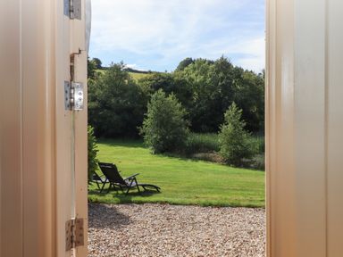 A garden with lounge chairs on grass viewed through an open door at Shepherds Joy Kennerleigh near Cheriton Fitzpaine