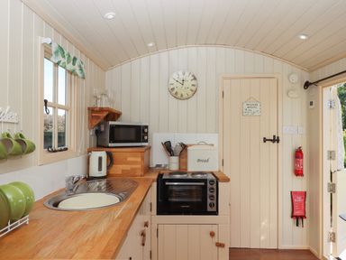 A small kitchen with a wooden countertop a sink microwave kettle bread box and a door with a wash room sign at Shepherds Joy Kennerleigh near Cheriton Fitzpaine
