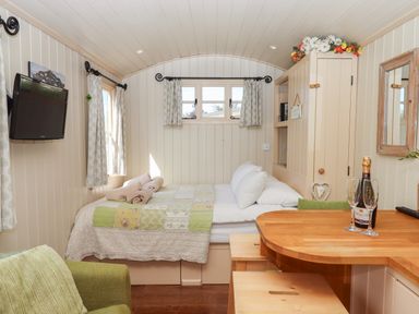 A small bedroom with a bed towels on it a wall-mounted tv a wooden table with two glasses and a bottle and a green chair at Shepherds Joy Kennerleigh near Cheriton Fitzpaine