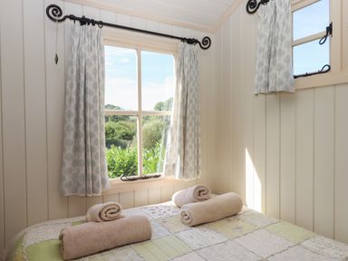 A bedroom with two windows and three rolled towels on a bed at Shepherds Joy in Kennerleigh near Cheriton Fitzpaine