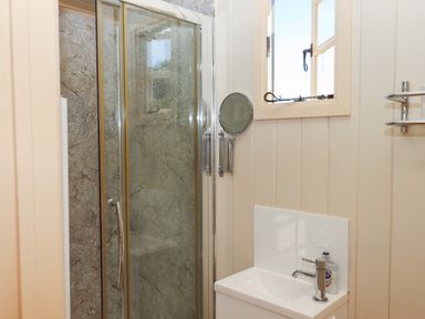 A bathroom with a glass shower enclosure a white sink with a chrome faucet a round wall-mounted mirror and a window at Shepherds Joy in Kennerleigh near Cheriton Fitzpaine