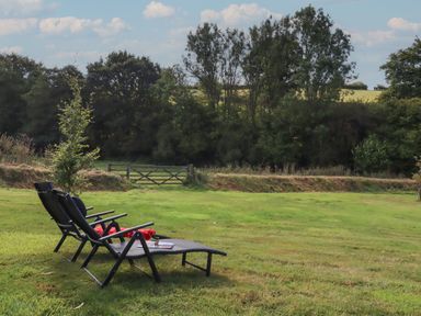 Two lounge chairs on a grassy lawn facing trees and a wooden gate at Shepherds Joy in Kennerleigh near Cheriton Fitzpaine
