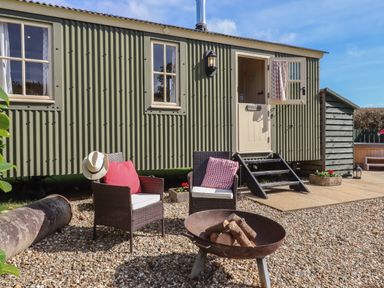 An outdoor seating area with two chairs and a fire pit in front of a green corrugated metal cabin at Shepherds Bliss in Kennerleigh near Cheriton Fitzpaine