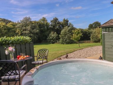 An outdoor seating area with a table and chairs next to a hot tub and a garden with trees at Shepherds Bliss in Kennerleigh near Cheriton Fitzpaine