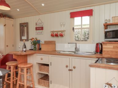 A kitchen with a wooden countertop a sink two bar stools a window with a red blind and kitchenware at Shepherds Bliss in Kennerleigh near Cheriton Fitzpaine