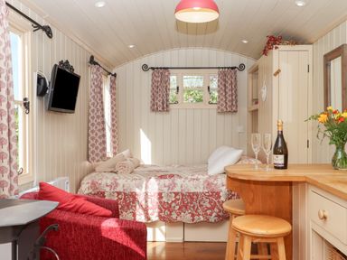 A small room with a bed a wooden counter with stools a red armchair and a wall-mounted television at Shepherds Bliss in Kennerleigh near Cheriton Fitzpaine