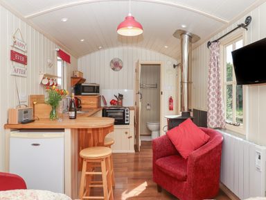 A small kitchen and living area with a wooden counter, red armchair, stove, and a door to a bathroom at Shepherds Bliss Kennerleigh near Cheriton Fitzpaine