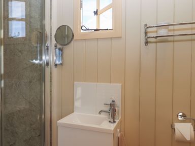 A bathroom with a shower, small sink with a faucet, hand soap bottle, mirror, towel rack, and toilet paper holder at Shepherds Bliss in Kennerleigh near Cheriton Fitzpaine