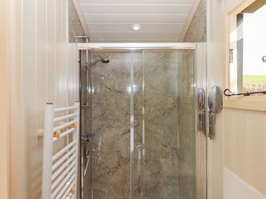 A shower enclosure with glass sliding doors a mounted shower head and a towel radiator in a bathroom at Shepherds Bliss Kennerleigh near Cheriton Fitzpaine