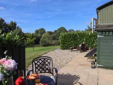 A patio with a table set with croissants and orange juice near a green garden shed and a lawn at Shepherds Bliss in Kennerleigh near Cheriton Fitzpaine