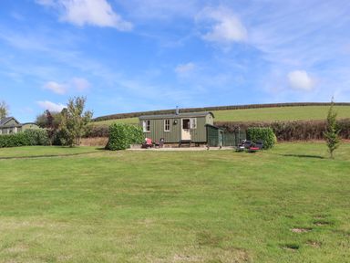 A small green cabin with chairs and a grassy field at Shepherds Bliss in Kennerleigh near Cheriton Fitzpaine