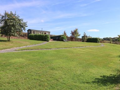 A grassy lawn with pathways trees two small cabins and chairs at Shepherds Bliss Kennerleigh near Cheriton Fitzpaine