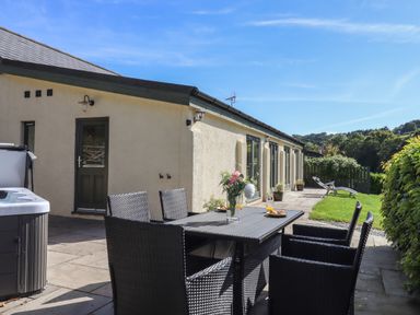An outdoor patio with a dining table and chairs a hot tub and a lawn at Binneford Barn in Kennerleigh near Cheriton Fitzpaine