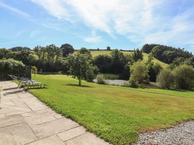 A patio with lounge chairs overlooking a grassy lawn with trees and hills in the background at Binneford Barn Kennerleigh near Cheriton Fitzpaine