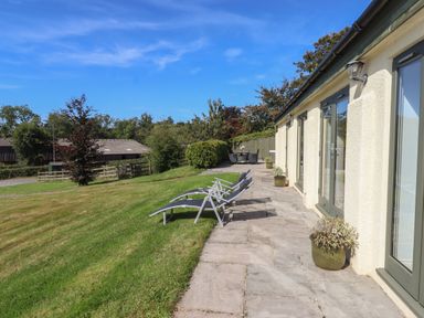 A patio with lounge chairs and potted plants beside a building with glass doors and a lawn at Binneford Barn Kennerleigh near Cheriton Fitzpaine