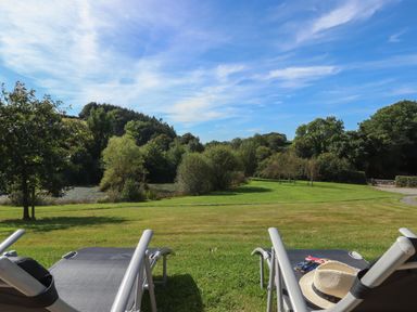 A garden with lawn chairs overlooking a grassy area with trees and a hill at Binneford Barn in Kennerleigh near Cheriton Fitzpaine