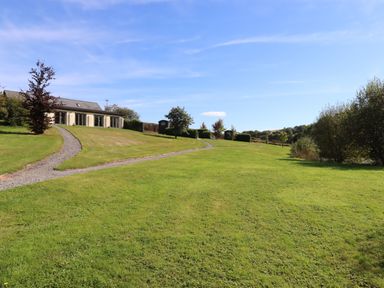 A large grassy yard with a gravel path leading to a house and small sheds at Binneford Barn in Kennerleigh near Cheriton Fitzpaine
