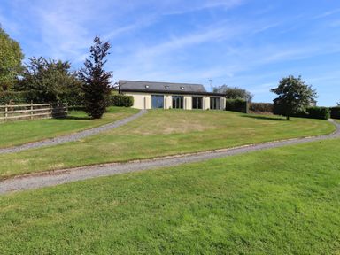 A single story building with large windows and a gravel path on a grassy hill at Binneford Barn in Kennerleigh near Cheriton Fitzpaine