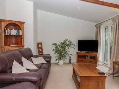 A living room with a brown leather sofa a wooden coffee table a TV on a wooden stand a bookshelf and a plant at Binneford Barn Kennerleigh near Cheriton Fitzpaine