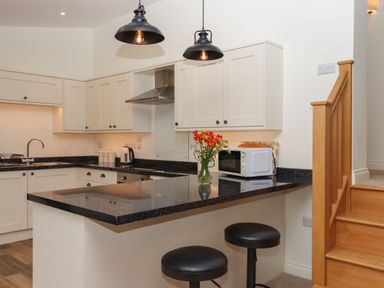 A kitchen with black countertops white cabinets a microwave flowers on the counter and two stools at Binneford Barn in Kennerleigh near Cheriton Fitzpaine