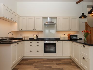 A kitchen with cream cabinets black countertops a stainless steel oven a kettle a microwave and flowers in a vase at Binneford Barn Kennerleigh near Cheriton Fitzpaine