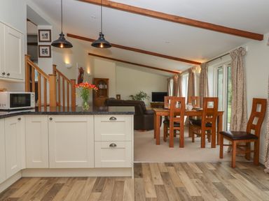 Kitchen with cupboards and countertop opening to dining area with wooden table and chairs and living room with sofa and television at Binneford Barn in Kennerleigh near Cheriton Fitzpaine