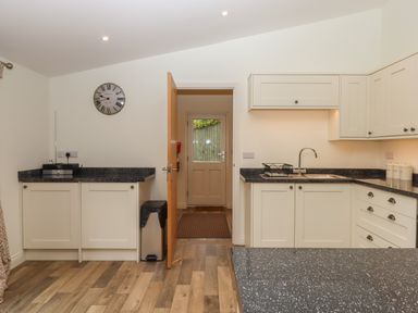 A kitchen with white cabinets black countertops a wall clock and an open door at Binneford Barn in Kennerleigh near Cheriton Fitzpaine