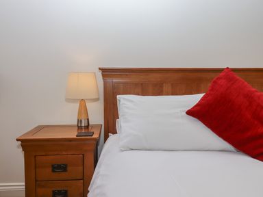 A wooden bedside table with a lamp next to a wooden bed headboard with white pillows and a red cushion at Binneford Barn Kennerleigh near Cheriton Fitzpaine