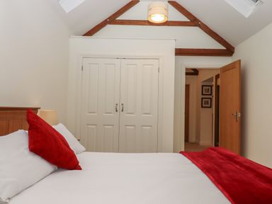 A bedroom with a white bed and red pillows and blanket wooden beams on the ceiling and wardrobe with double doors at Binneford Barn Kennerleigh near Cheriton Fitzpaine