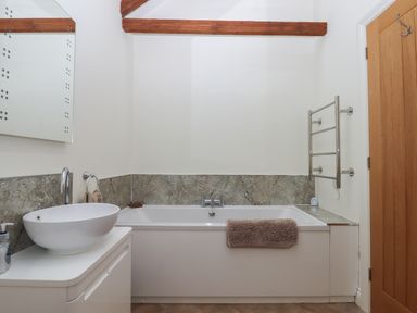 A bathroom with a bathtub a sink a mirror a wooden door and exposed wooden beams at Binneford Barn in Kennerleigh near Cheriton Fitzpaine