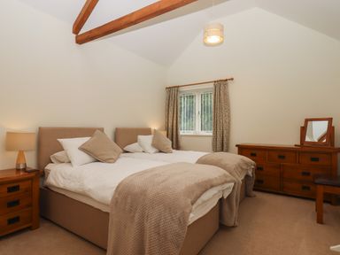 A bedroom with two single beds a wooden dresser a nightstand with a lamp and a window with curtains at Binneford Barn in Kennerleigh near Cheriton Fitzpaine